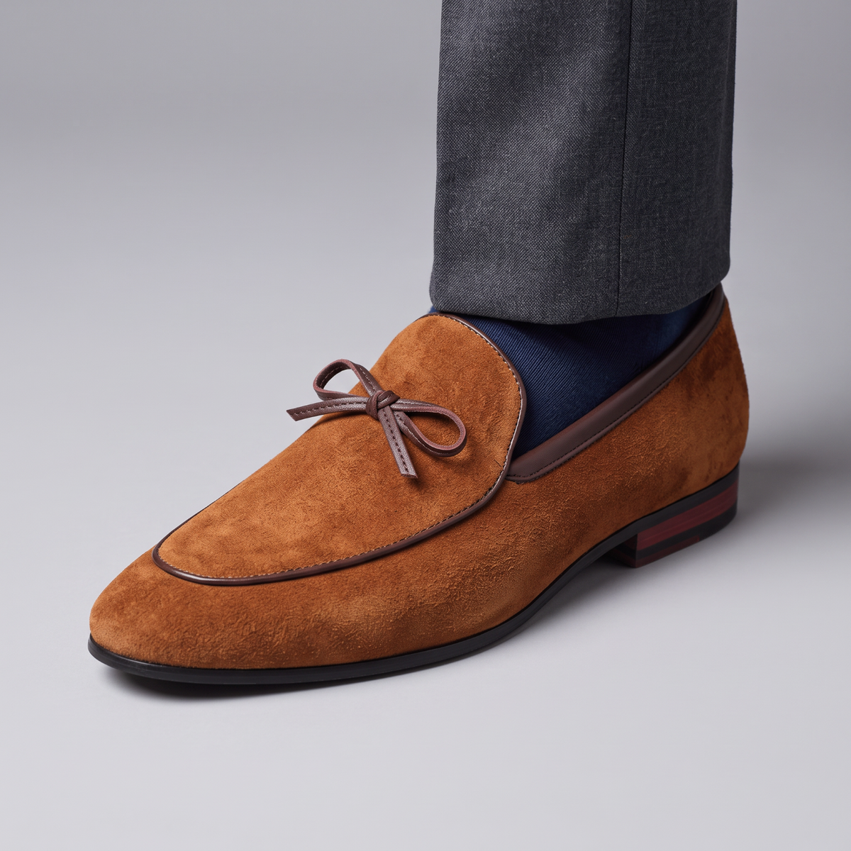 Mocassin Paris homme en daim marron avec détail de nœud, porté avec un pantalon gris pour une tenue habillée.