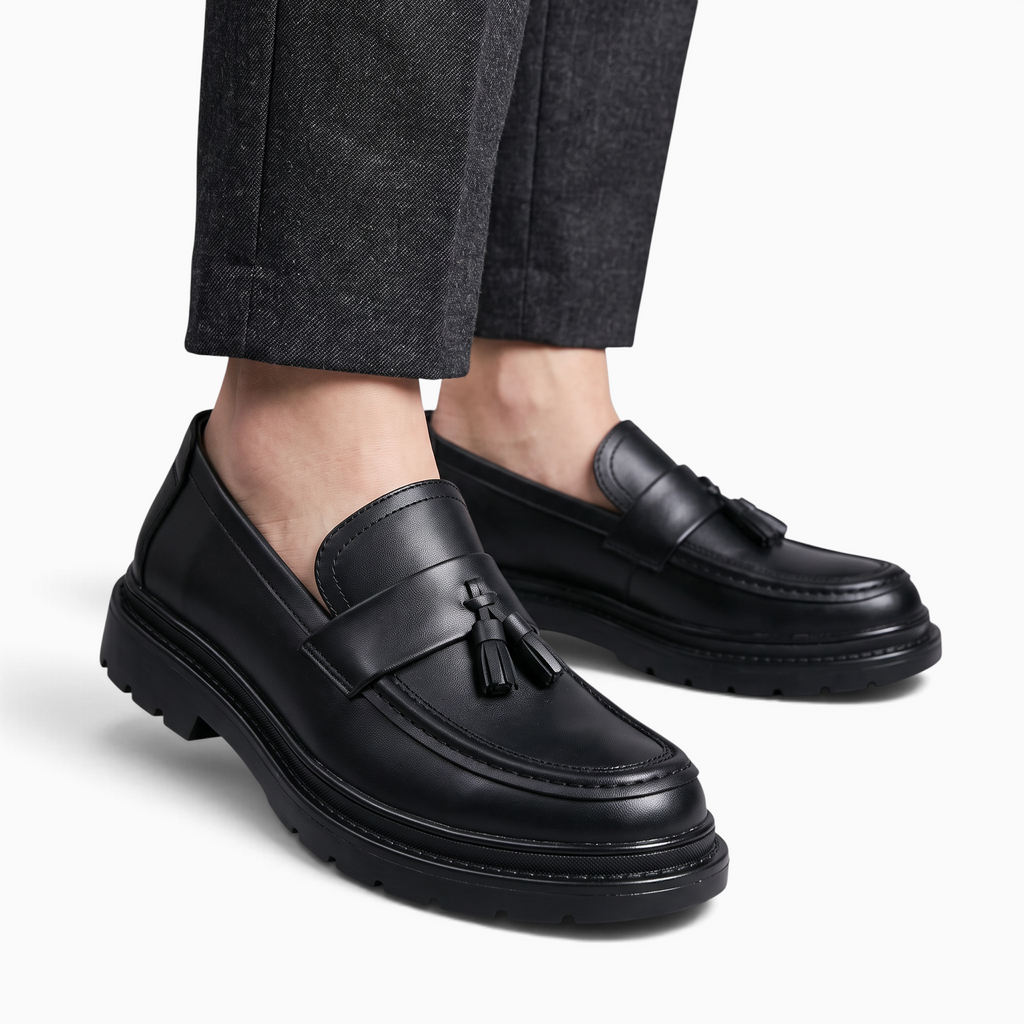 Mocassin Paris homme en cuir noir mat avec glands décoratifs et semelle plateforme épaisse portée avec un pantalon gris