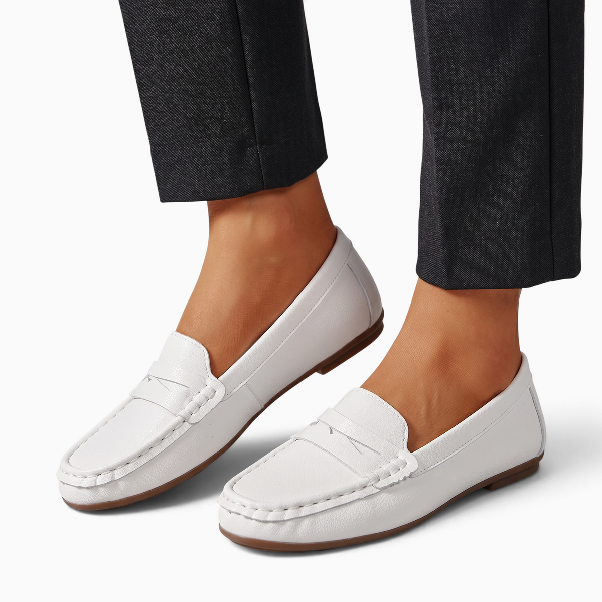 Mocassin Paris femme blanc en matière synthétique avec bout rond et semelle plate, porté avec un pantalon sombre.