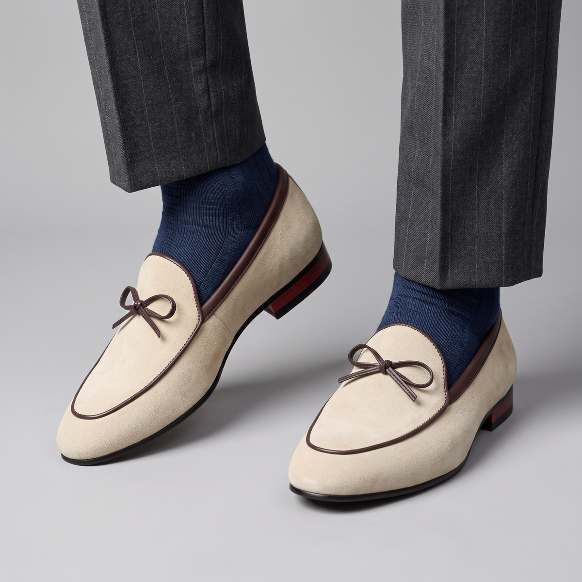 Mocassin Paris homme en daim beige avec liseré marron et nœud décoratif, porté avec un pantalon gris et chaussettes bleu