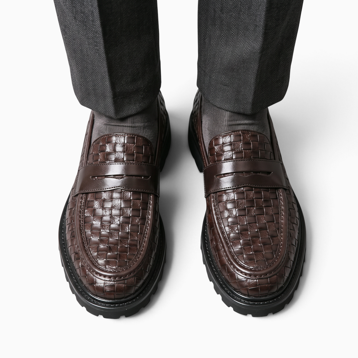Mocassin Paris marron en cuir tressé avec semelle crantée épaisse, porté avec un pantalon de costume gris.