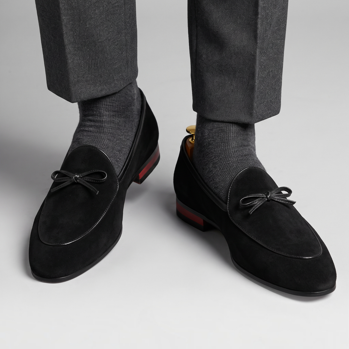 Mocassin Paris homme en daim noir avec détail de nœud sur le dessus, porté avec un pantalon gris pour une cérémonie.